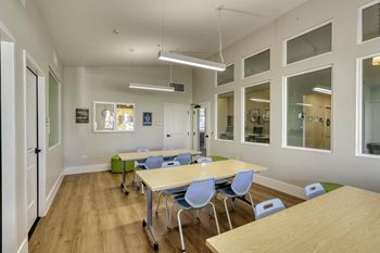 A room with tables and chairs and a white wall.